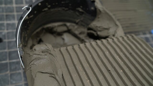 Tiled floor with fresh grey adhesive combed with notched trowel next to black bucket, home improvement and renovation