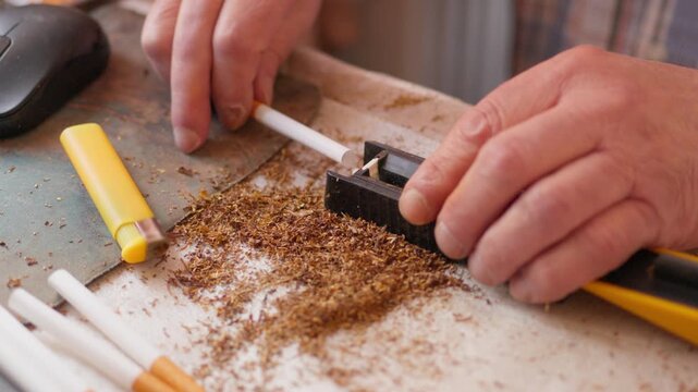 Close up of a person using a manual cigarette rolling machine to fill an empty paper tube with tobacco