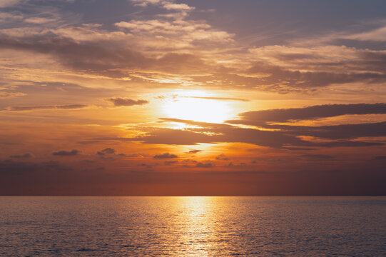 Sunset sun glowing over calm ocean expanse with clouded sky