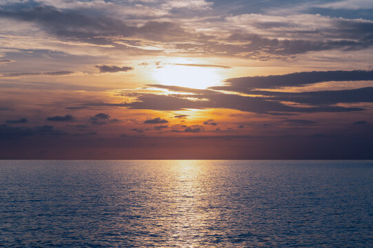 Ocean reflecting setting sun beneath layered clouds over sea
