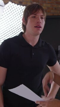 Vertical video: Accepting pages from coworker, man in black polo reviewing and pointing in studio