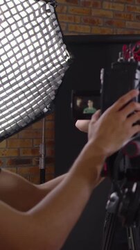 Vertical video: Seeing flip LCD, tech tweaking rig and framing model on set in green sweater, jeans