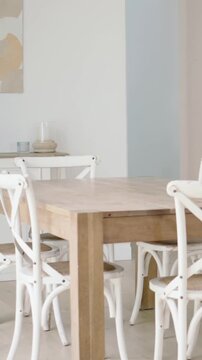 Vertical video: Panning camera left revealing wood table with white chairs in home and wall niche