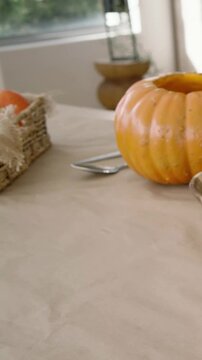 Vertical video: Panning pumpkin sliding on linen by window greenery, with basket, spoon, bowl, lamp