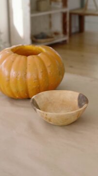 Vertical video: Moving cam revealing hollow pumpkin near window, with bowl and scissors for carving