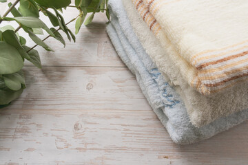 Neatly folded and stacked clean bath towels with eucalyptus leaves on white wooden background with copy space for organic lifestyle. © PH_BRICK