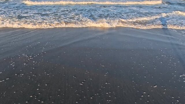 4K video looks down at Atlantic surf washing over dark coastal sand.