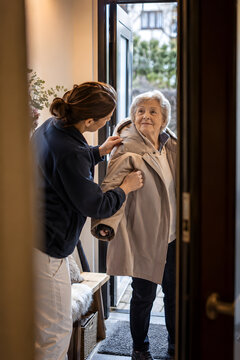 Caregiver helping an elderly woman put on a coat before an outdoor walk, capturing compassionate home care, independent aging, daily assistance and dignified senior mobility in warm natural light.