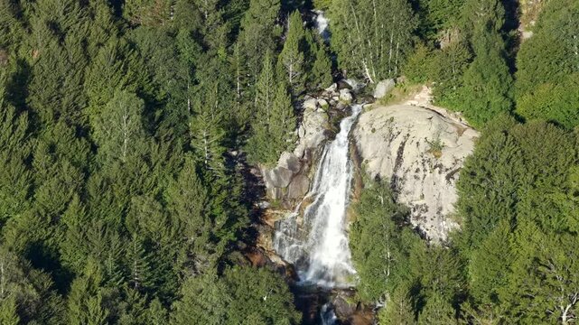 Aerial view of Cascada de Molieres waterfall cascading through alpine forest and granite mountain peaks, Val d'Aran, Pyrenees, Spain