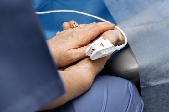 Patient's hands with a pulse oximeter attached to a finger during a medical procedure. Blood oxygen monitoring.