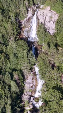 Aerial view of Cascada de Molieres waterfall cascading through alpine forest and granite mountain peaks, Val d'Aran, Pyrenees, Spain