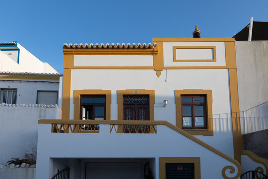 White house facade with ochre trim and traditional tiled roof under clear blue sky in Ferragudo, Portugal