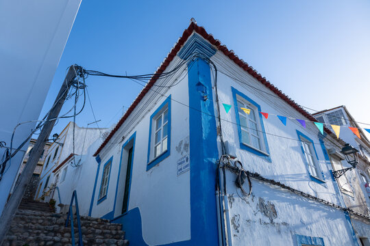White house with blue trim and colorful bunting on a narrow street in Ferragudo, Portugal