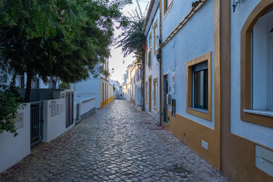 Narrow cobblestone street lined with blue and yellow houses in Ferragudo, Algarve, Portugal at dusk