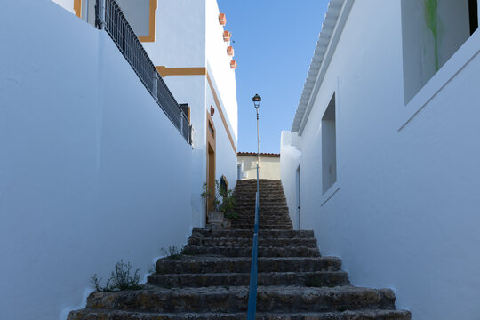 Narrow stone staircase between whitewashed houses with orange trim under a blue sky in Ferragudo, Portugal