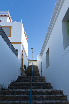 Narrow stone staircase between whitewashed houses under a clear blue sky in Ferragudo, Portugal