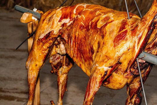 Golden brown whole roasted lamb on a spit at a traditional barbecue.