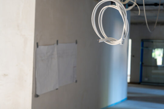 Wider selective-focus view with a looped cable at upper right, two pinned paper sheets on a grey wall and an empty hallway fading into soft blue light.