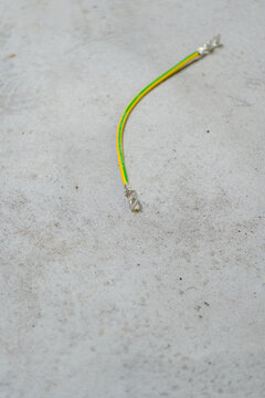 An isolated piece of standard yellow and green grounding cable with metal ring terminals at both ends, resting on a textured grey concrete floor during construction work.