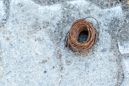 A heavily oxidized roll of steel wire resting on rough concrete, representing industrial decay, discarded construction materials, or rugged outdoor textures.
