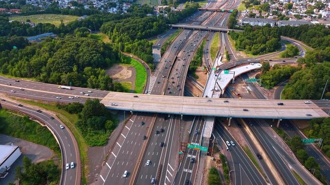 Large interchange with lots of quickly moving cars. Green woods and rural cityscape are around the highway.
