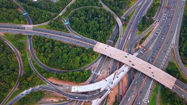 Complex highway interchange of intersecting roads and sweeping flyover ramps. Dense clusters of deep green trees fill the pockets of land between the motorways.