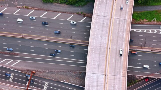 Descending on the concrete overpass above the multi-lane highway system. Cars move quickly by the numerous roads.
