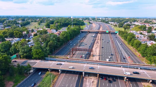 Modern massive multi-lane highway system with numerous moving cars. Motorway winding through a verdant landscape under a bright, partly cloudy sky.