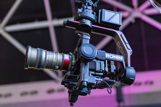 Amsterdam, Netherlands - September 11, 2026: Professional Ronin cinema camera with large zoom lens and monitor suspended before illuminated exhibition truss at IBC media technology event