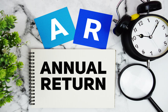 AR Annual Return text written on notepad with alarm clock and magnifying glass on marble background
