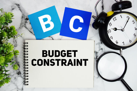 BC Budget Constraint text written on notepad with alarm clock and magnifying glass on marble background