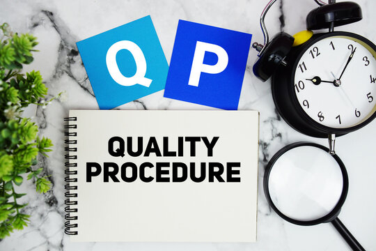 QP Quality Procedure text written on notepad with alarm clock and magnifying glass on marble background