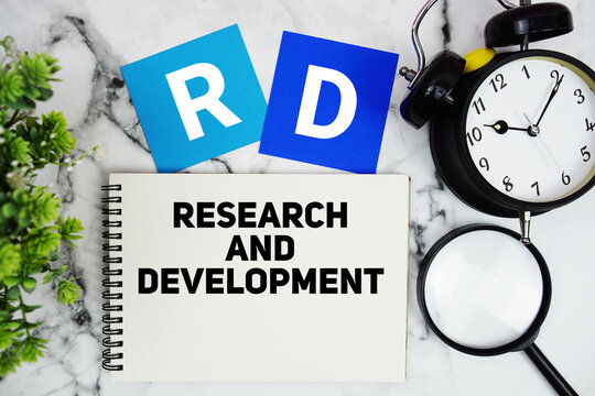 RD Research and Development text written on notepad with alarm clock and magnifying glass on marble background