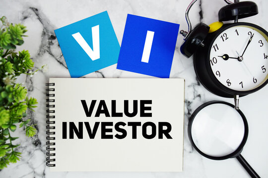 VI Value Investor text written on notepad with alarm clock and magnifying glass on marble background