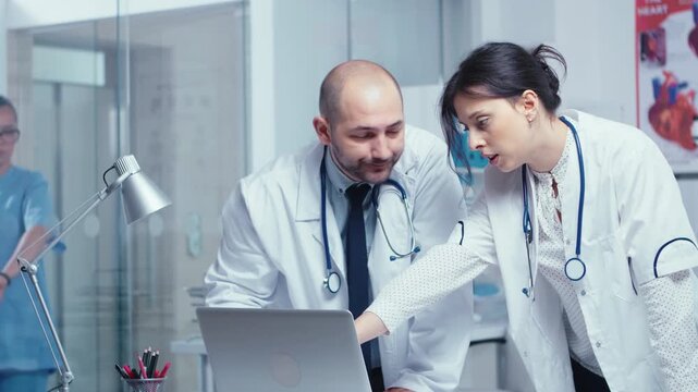Two physicians discuss a medical issue at a laptop as the woman gestures toward the screen, combining professional debate with collaborative problem solving, reinforcing clinical teamwork.
