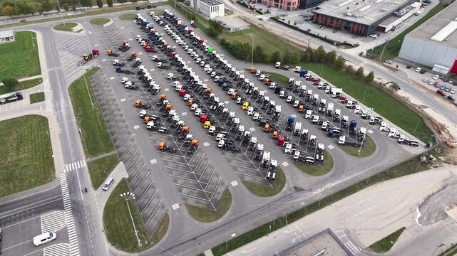 Aerial view of rows of parked new trucks and commercial vehicles in a large paved parking lot with colorful cabs and marked spaces. Drone footage of warehouse of manufactured lorry cars. Industrial co