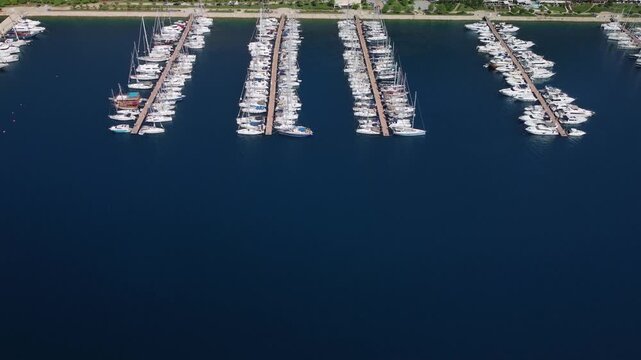 Aerial coastal city marinas with multiple piers and beachfront road with green spaces and pedestrian promenade. Boats lined in parallel slips. Urban planning perspective. Tourism and infrastructure