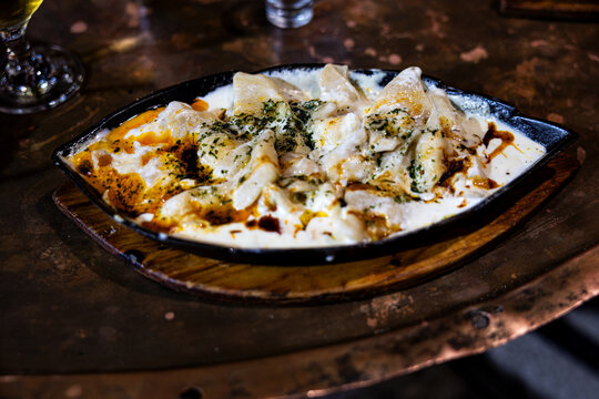 Traditional Bosnian Klepe dumplings with garlic cream sauce, melted butter and paprika in a hot skillet. Sarajevan cuisine.