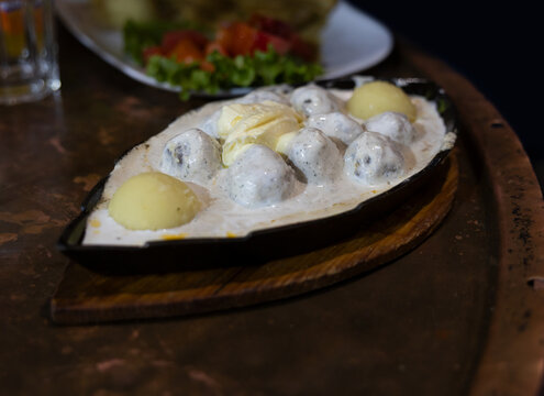 Traditional Bosnian meatballs (Cufte) in a rich cream sauce with boiled potatoes, served hot in a cast iron pan. Sarajevo local food.