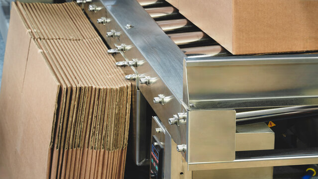 Elements of corton boxes collected in stack. Conveyor line for production of boxes. Machine cuts cardboard boxes from sheets of cardboard. Enterprise for production package.