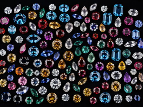 An opulent collection of brilliant, faceted gemstones in a dazzling array of colors and shapes, artfully arranged on a deep black surface.