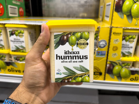 Prosper, Texas, USA - September 16th, 2026: Person holding Ithaca hummus olive oil sea salt container helf inside Costco warehouse store