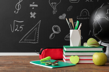 Education and back to school concept, classroom desk with books and stationery supplies against a chalkboard with hand drawn math and science icons © Pixel-Shot