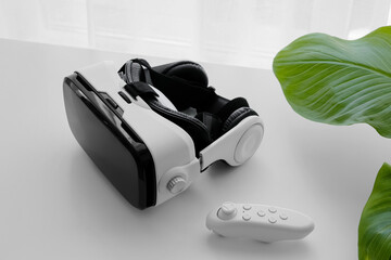 Virtual reality and metaverse technology, vr headset with controller for immersive gaming and digital simulation on a clean white desk with green leaves © Pixel-Shot
