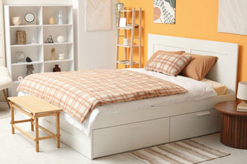 Home interior design and cozy bedroom decor, modern bed with storage drawers and plaid bedding in a bright room with orange accent wall and shelving © Pixel-Shot