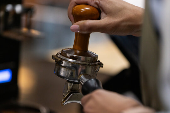 Asian mid-adult barista tamping coffee grounds with tamper into portafilter near espresso machine
