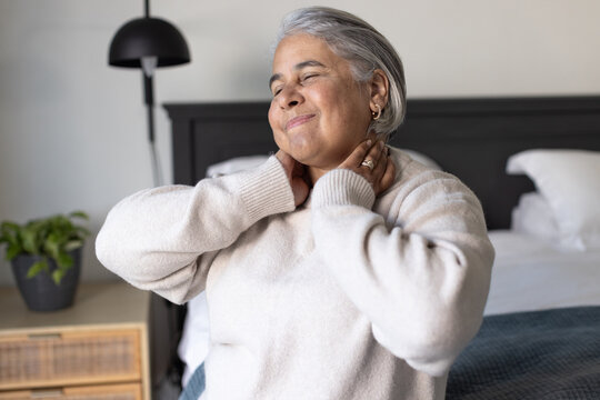 Senior African American woman sitting on bed in bedroom, touching neck showing rings