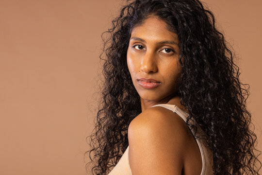 African American woman posing, turning over shoulder and meeting camera in studio with beige tank