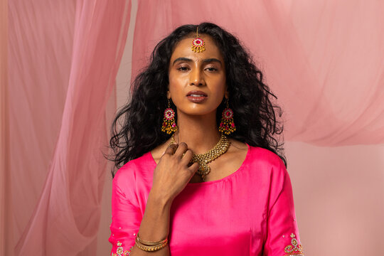 Adult Indian woman posing in studio wearing fuchsia tunic and adjusting gold choker, maang tikka