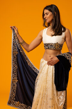 Indian woman modeling in studio holding navy embroidered drape, steadying cream lace skirt